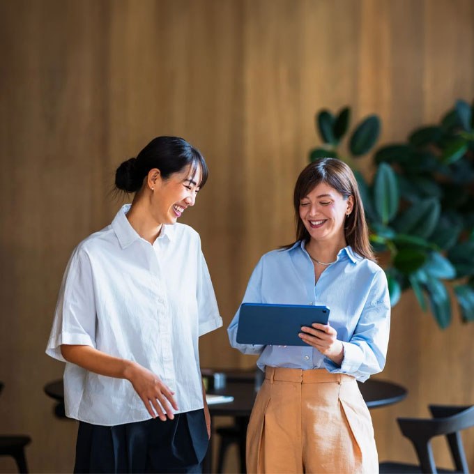 Two women sharing a moment over a tablet in a warm interior, Solance client and account director